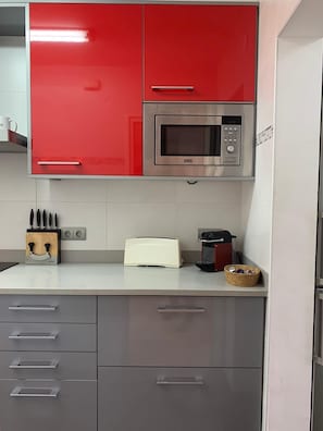 A kitchen with red cabinets, a microwave, a toaster, and a knife block. - Beach Apt: Huge 80m² Private Terrace, 2 Min Walk to Beach &  Free Parking (Tamariu)