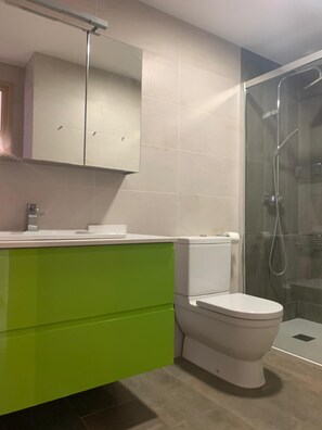 Ein Badezimmer mit Toilette, einem grünen Waschtisch, einem Spiegel und einer Glasdusche.