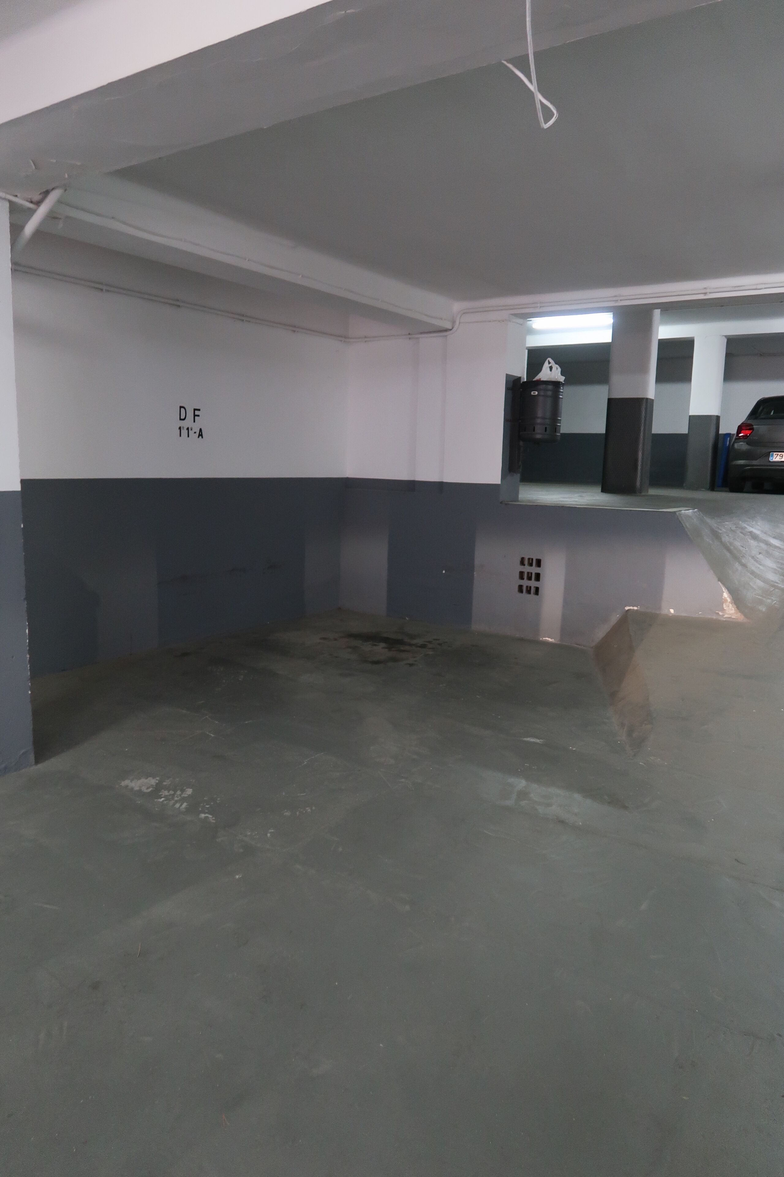 A parking garage with concrete floors and walls, a visible ceiling with exposed pipes, and a car parked in the background.