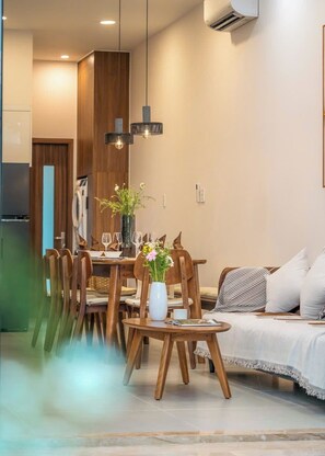 A modern dining area with a wooden table set for six, a sofa with a patterned throw, and a vase with flowers on a side table. - Private vacation house in An Thuong - beach-near (Đà Nẵng)