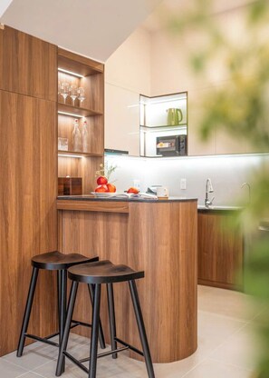 A modern kitchen with wooden cabinetry, a central island with stools, and built-in appliances. - Private vacation house in An Thuong - beach-near (Đà Nẵng)