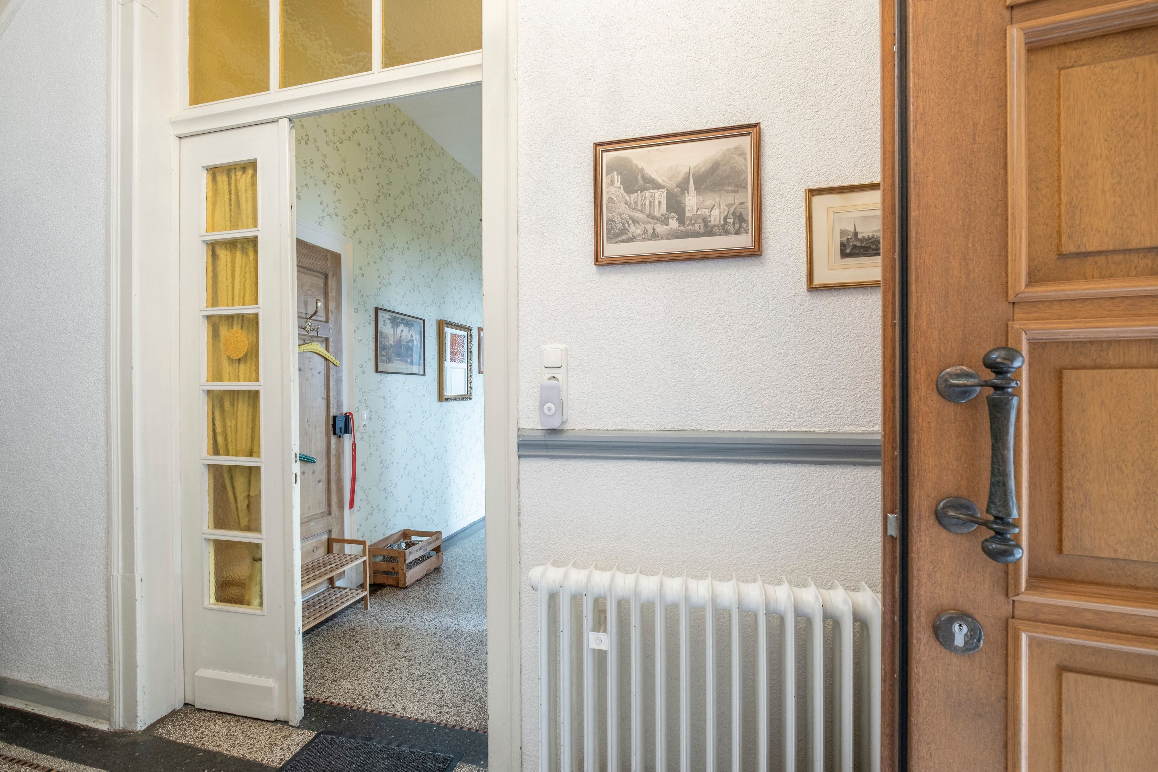 A hallway with a wooden door, a radiator, and a framed picture on the wall.