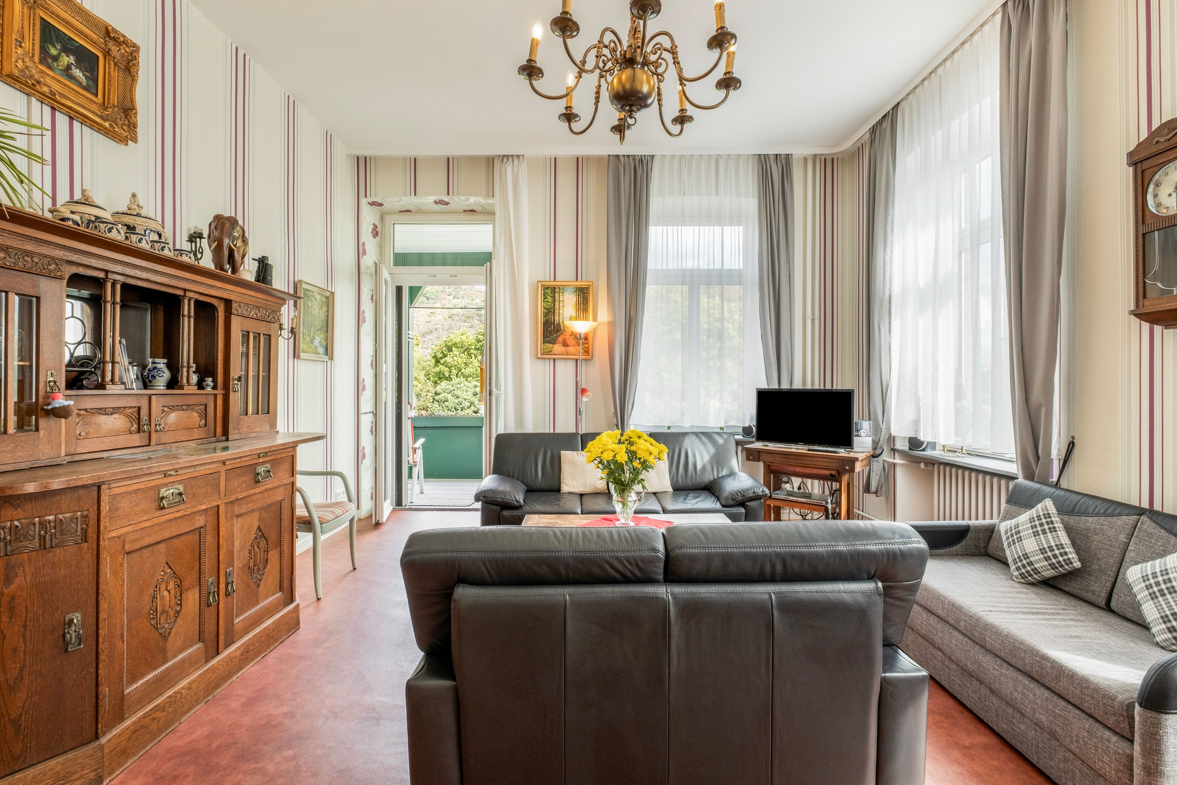 A living room with a sofa, a television, a wooden cabinet, and a chandelier.