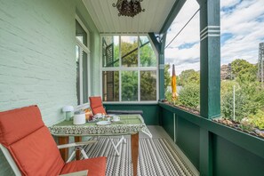 A small balcony with a table set for breakfast, a chair, and a view of greenery.