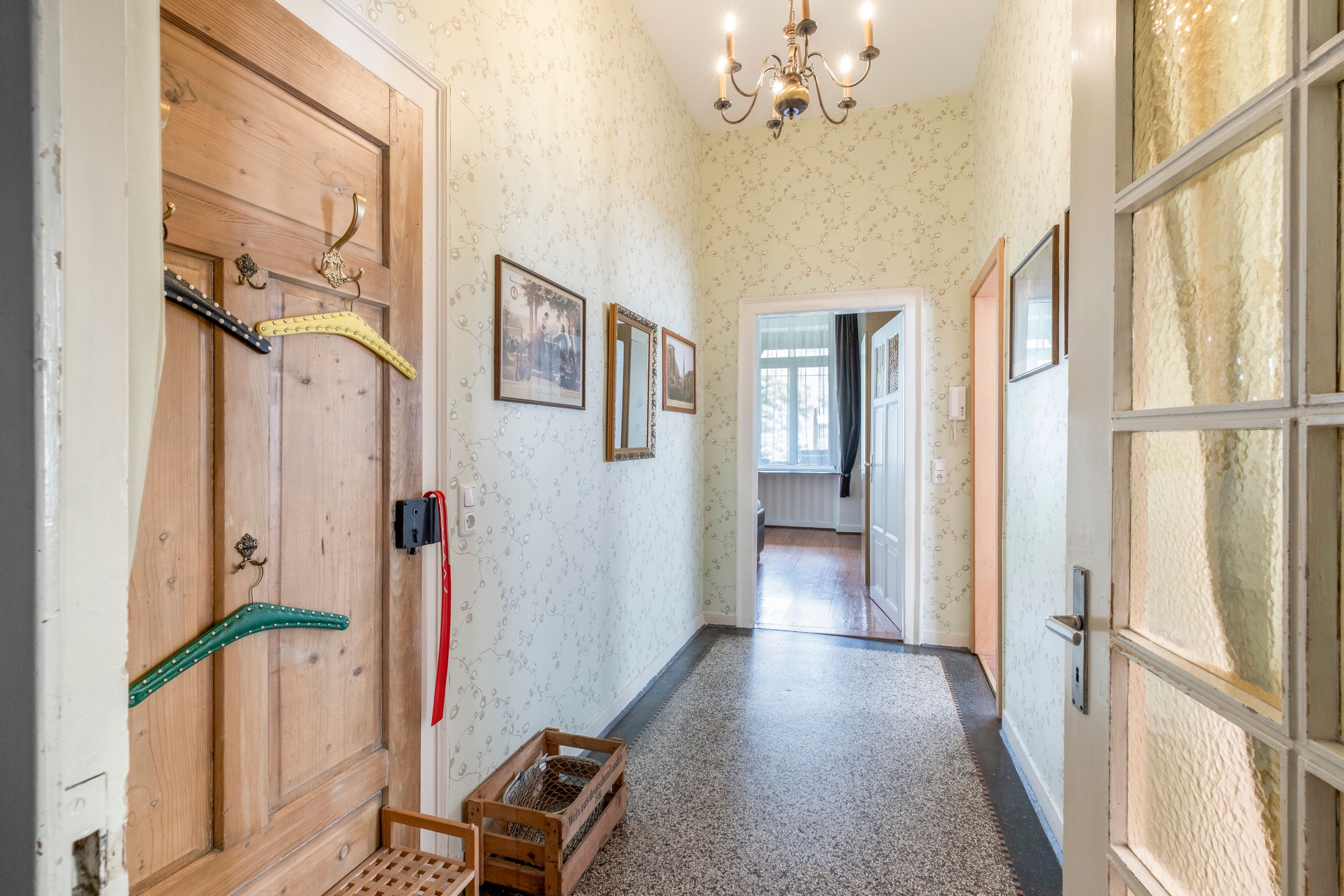 Ein Flur mit Holztüren, einem Chandelier, gerahmten Bildern an der Wand und einer Holzkiste auf dem Boden.