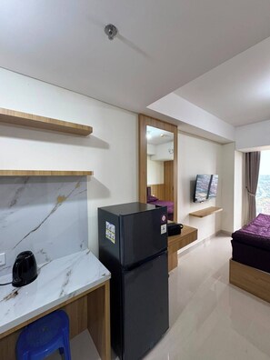 Ein Hotelzimmer mit einer Marmorplatte, einem schwarzen Kühlschrank, einem Bett mit violetter Bettdecke, einem Fernseher und einem Fenster mit Vorhängen.