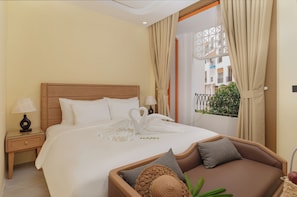 Ein Hotelzimmer mit einem großen Bett, einem Nachttisch mit Lampe, einer Couch mit Kissen und einem Fenster mit Vorhängen.