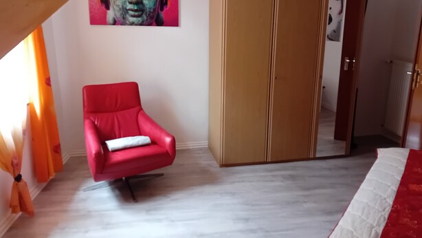 A room with a red chair, a wardrobe, and a painting on the wall.