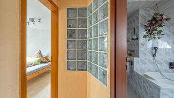 Un baño con ducha, inodoro y lavamanos. Cuenta con un ventanal con paneles de vidrio decorativo.