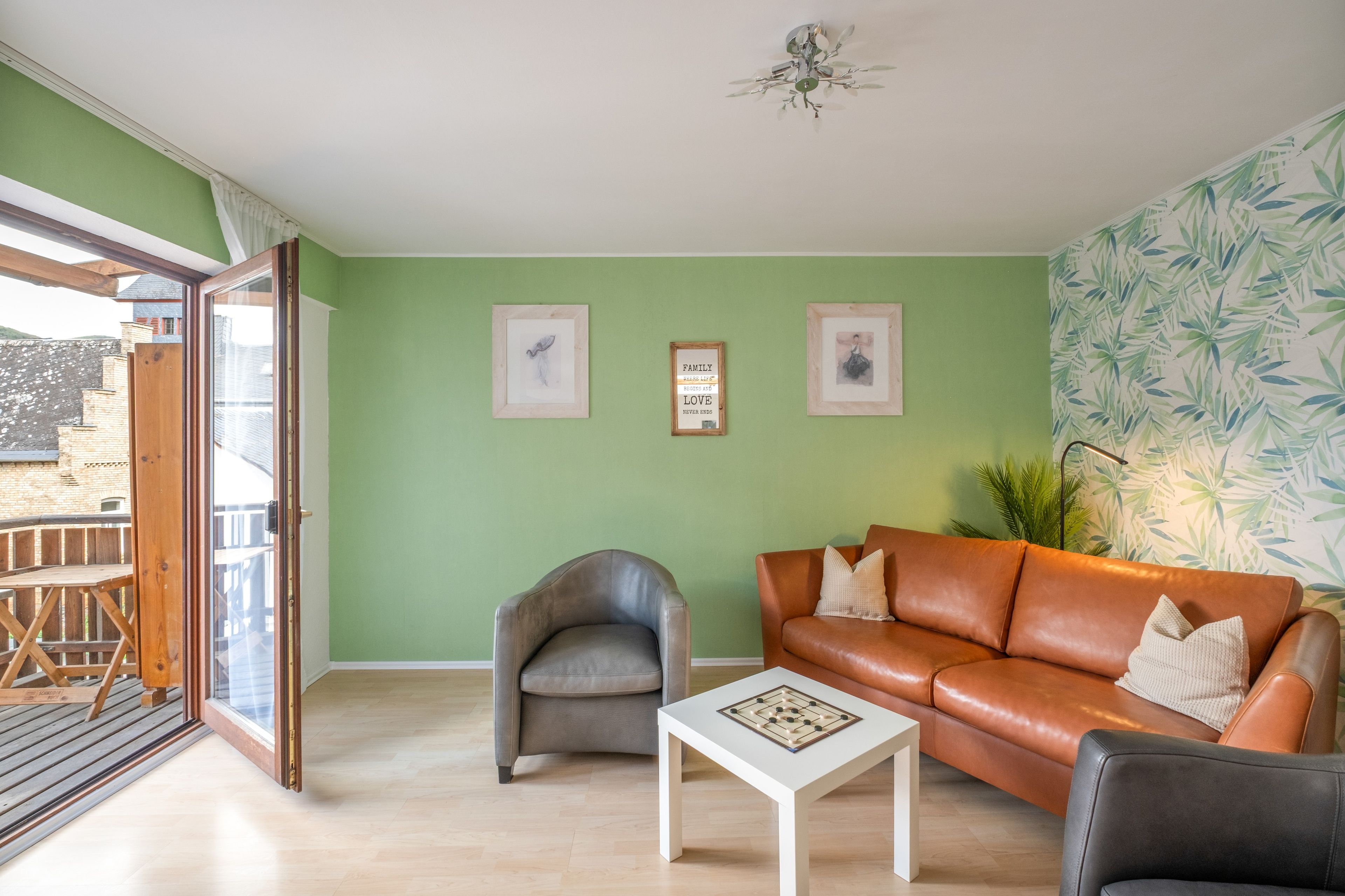 Ein Wohnzimmer mit grüner Wand, einem braunen Ledersofa, einem grauen Sessel, einem weißen Couchtisch und zwei gerahmten Bildern.