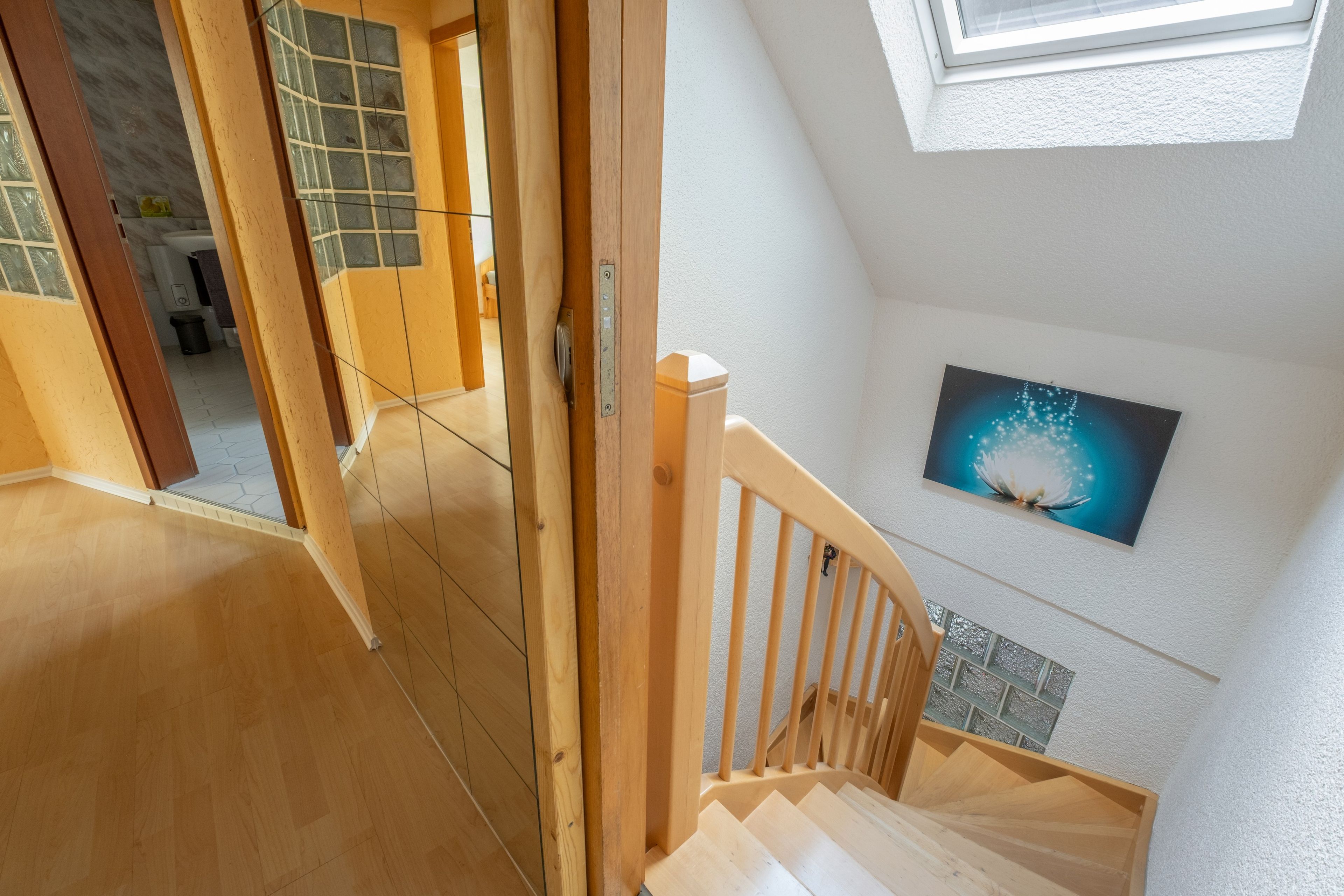 Eine Holztreppe führt zu einer Zwischenplattform mit Blick auf ein Badezimmer und ein an der Wand hängendes Bild.