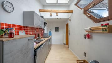A narrow kitchen with a skylight, a wooden beam ceiling, and a view through a window.