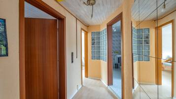 A hallway with wooden doors, a ceiling fan, and a view into a room with a bed and a window.