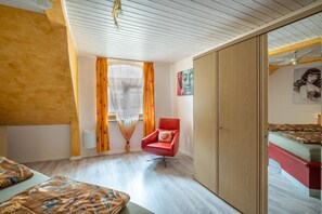 Une pièce avec un lit, une chaise rouge, une armoire et une fenêtre avec des rideaux.