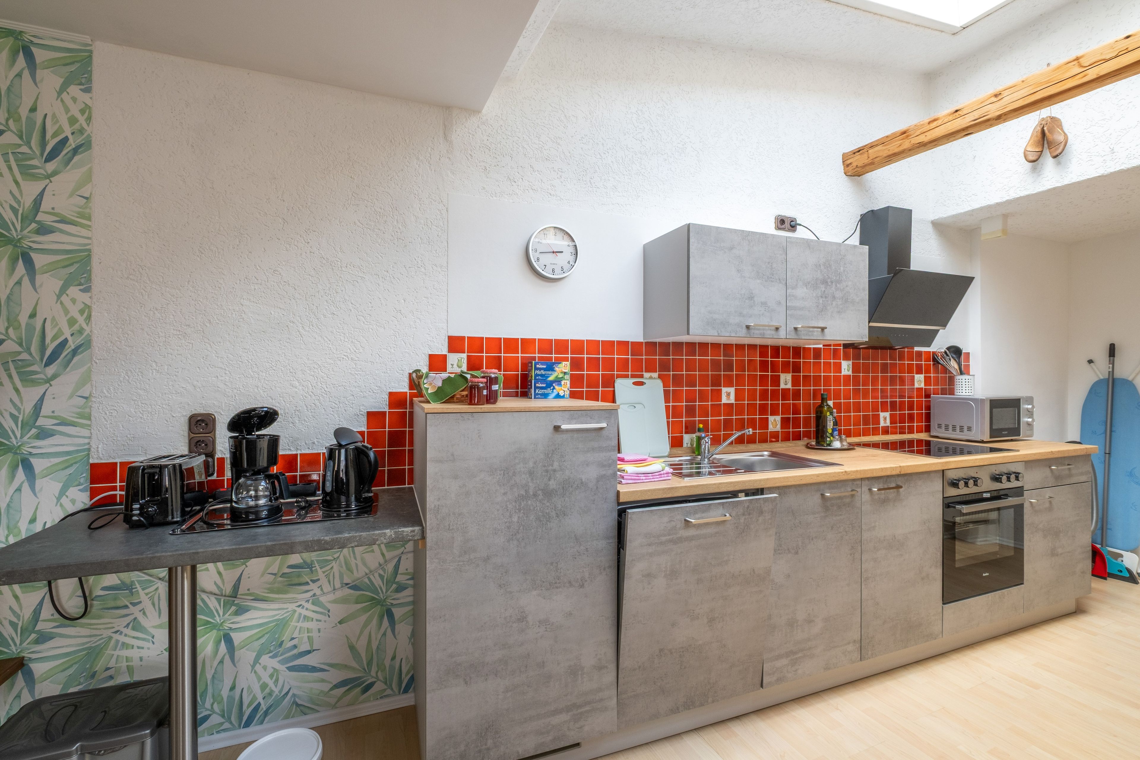 A modern kitchen with a wooden countertop, grey cabinets, a red-tiled backsplash, and a built-in oven.