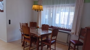 A dining area with a wooden table and chairs, a hanging lamp, and a window with curtains.