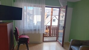 A living room with a television, a chair, a table with a board game, and a sliding glass door leading to a balcony.