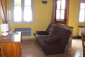 A room with a brown sofa, a wooden desk with a lamp, and a radiator. - Holiday Home “Gîte du Soleil Levant” with Private Garden and Wi-Fi (Saint-Valery-sur-Somme)