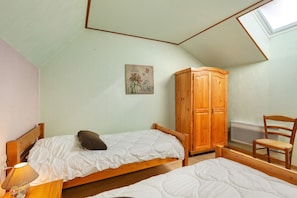 A bedroom with two beds, a wooden wardrobe, a chair, and a painting on the wall.