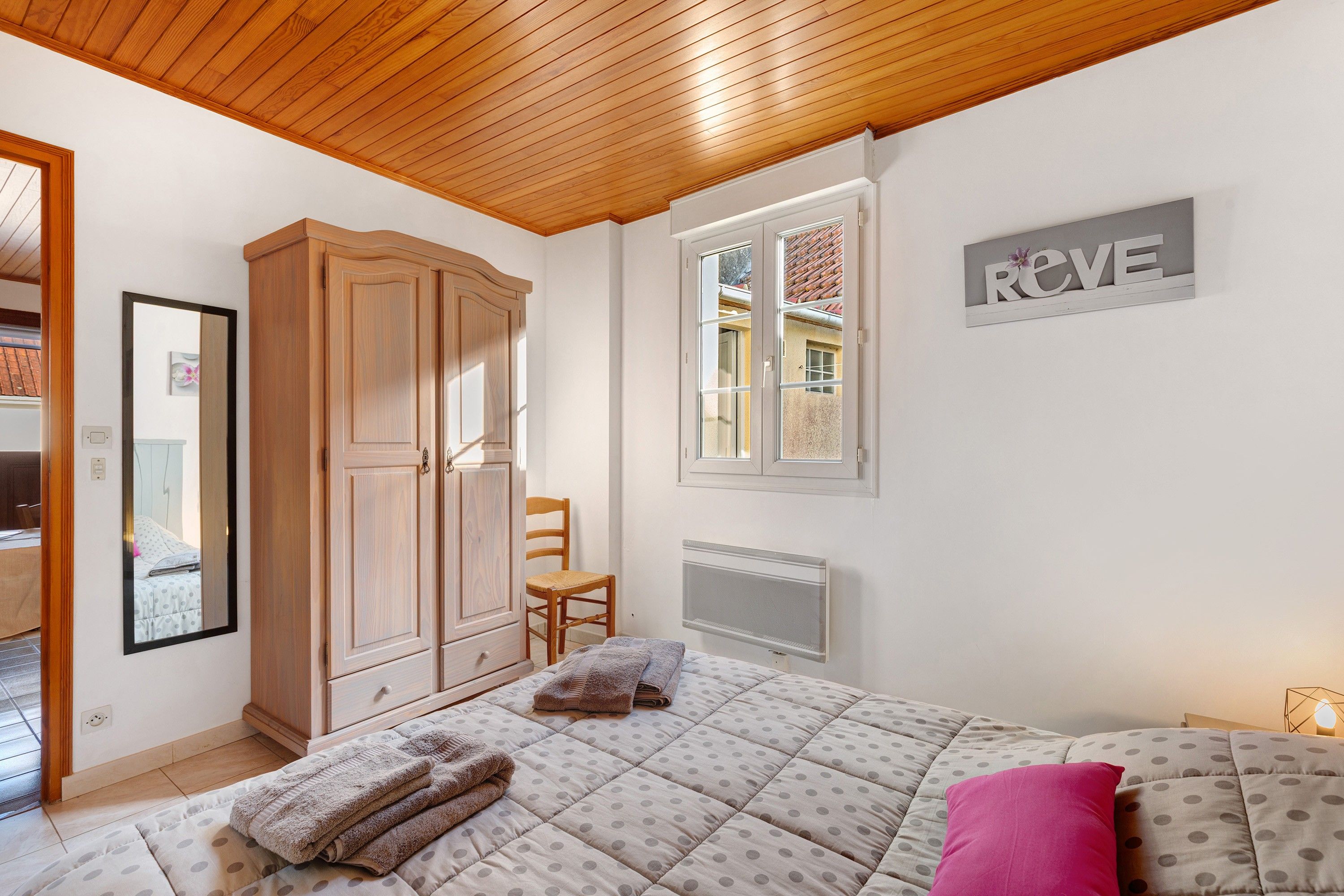 A bedroom with a bed, a wardrobe, a chair, a radiator, and a window with a view of the outside.