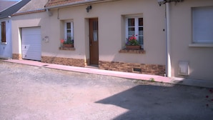 Un edificio residenziale con tetto in tegole rosse, un portone e due finestre con balconiere fiorite.