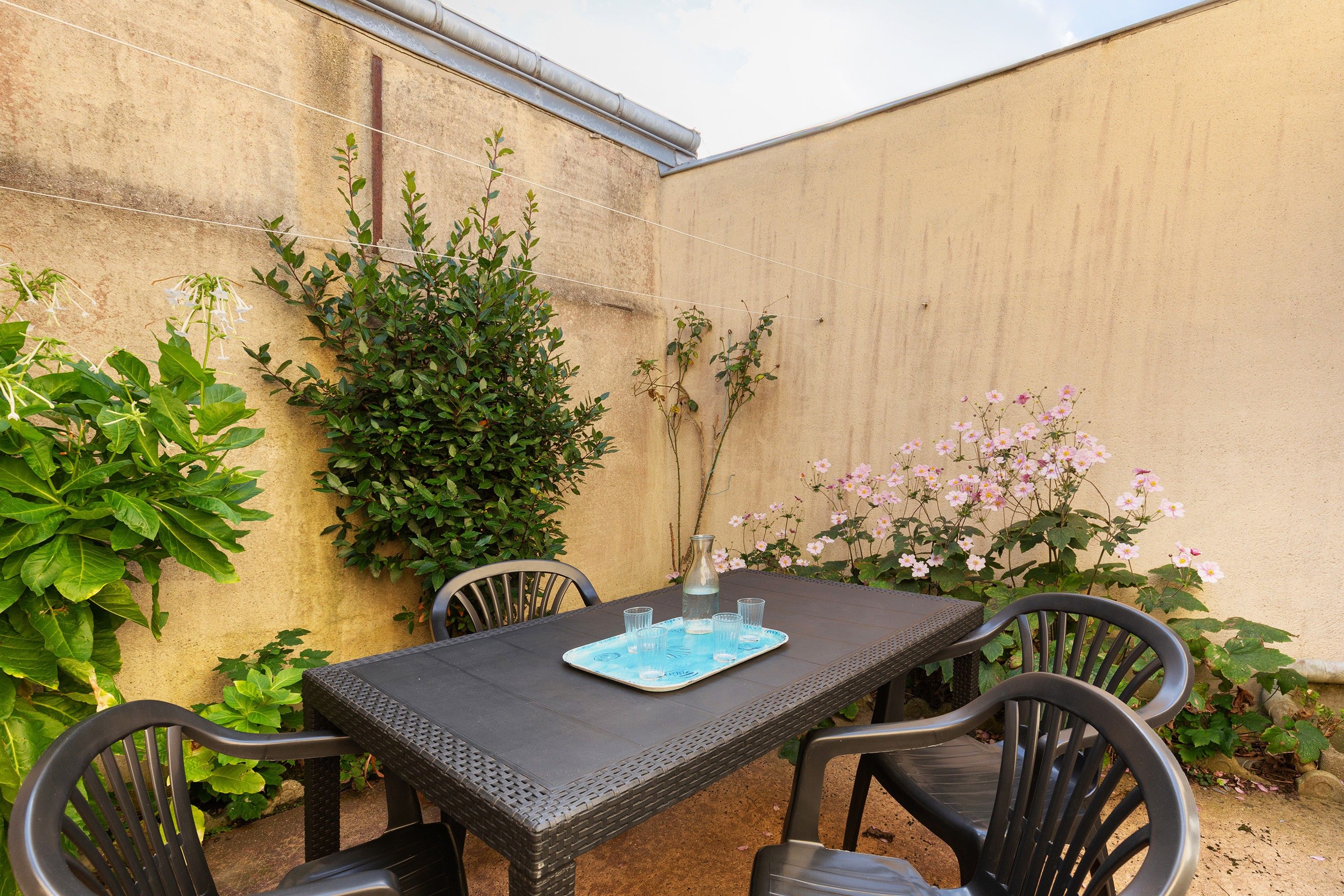 An outdoor patio with a table and chairs, surrounded by plants and flowers.