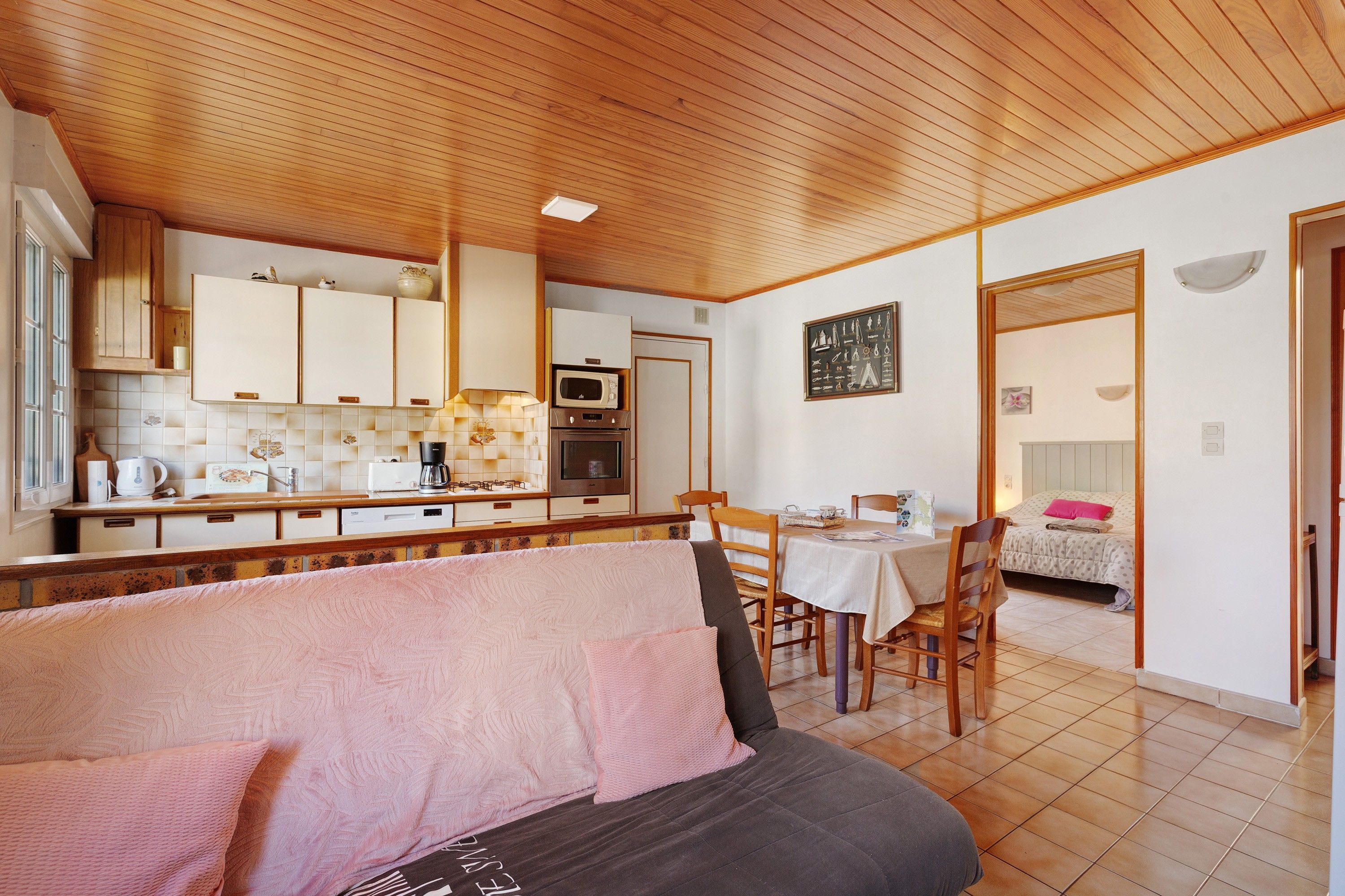 A cozy room with a bed, a dining table with chairs, a kitchen area with cabinets and appliances, and a bathroom visible through an open door.