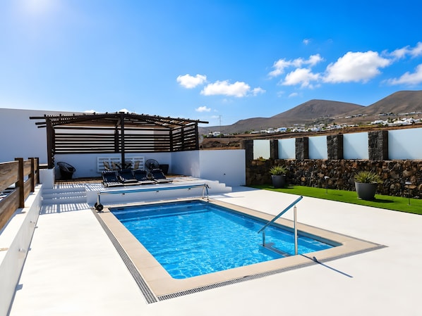 Una piscina al terrat amb una pèrgola, zona de seients i vistes a muntanyes llunyanes.