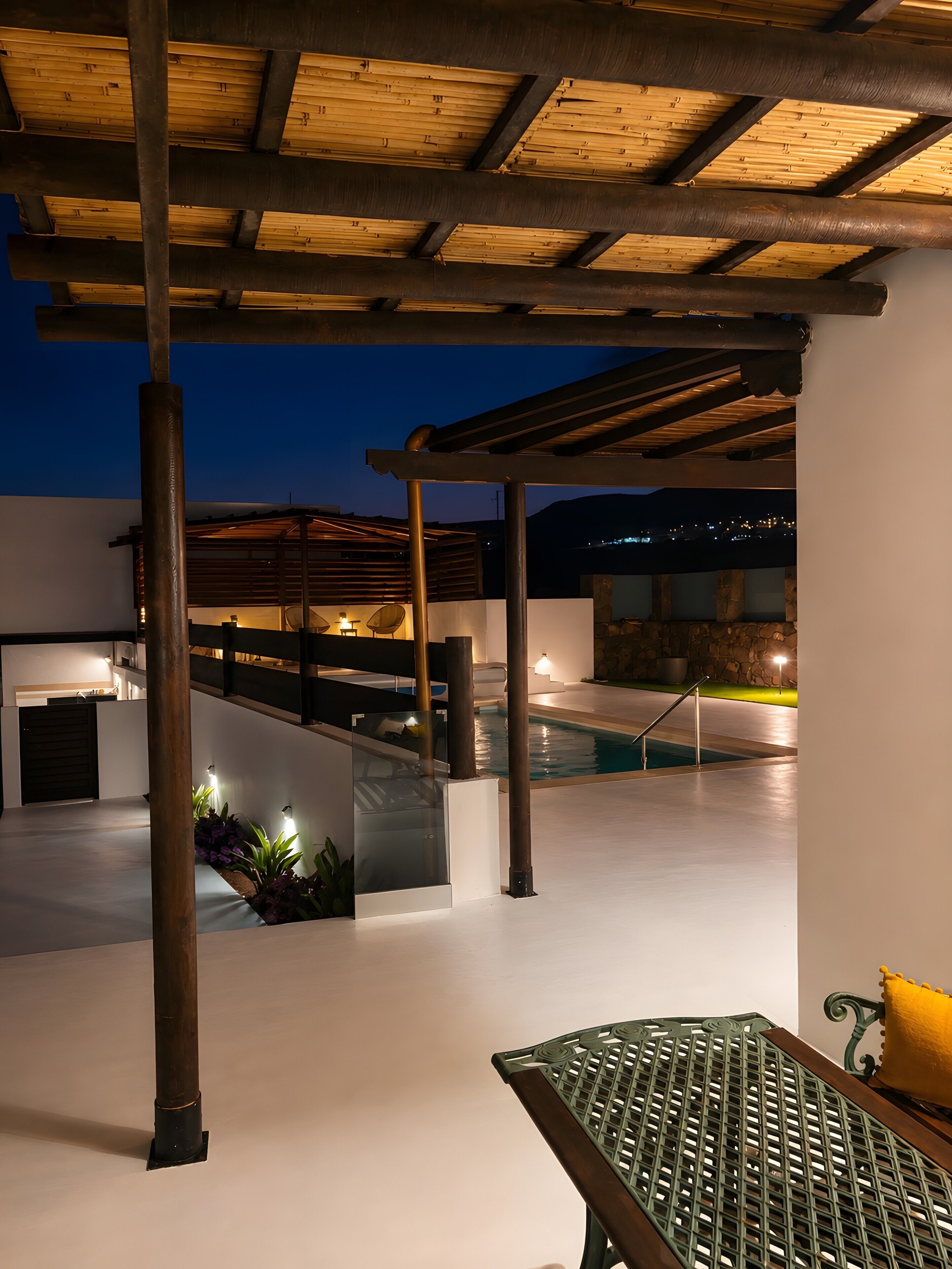 A rooftop pool area with a pergola, seating, and a view of the city at dusk.
