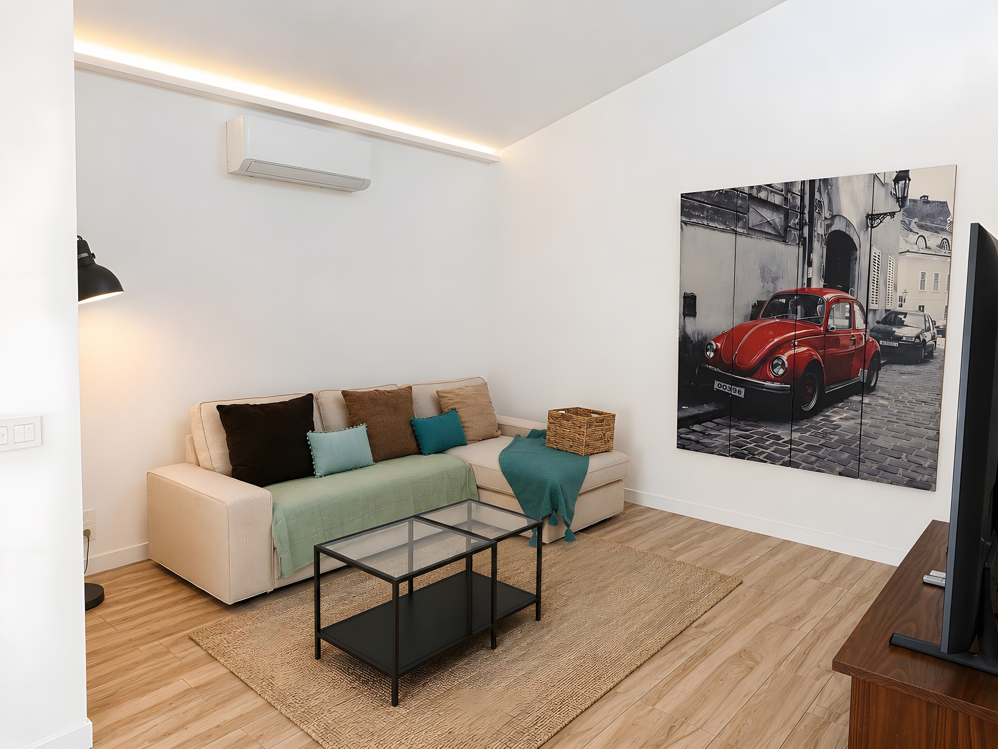 Una sala de estar moderna con un sofá, una mesa de centro de vidrio, un cuadro de un coche clásico y un televisor de pantalla plana.