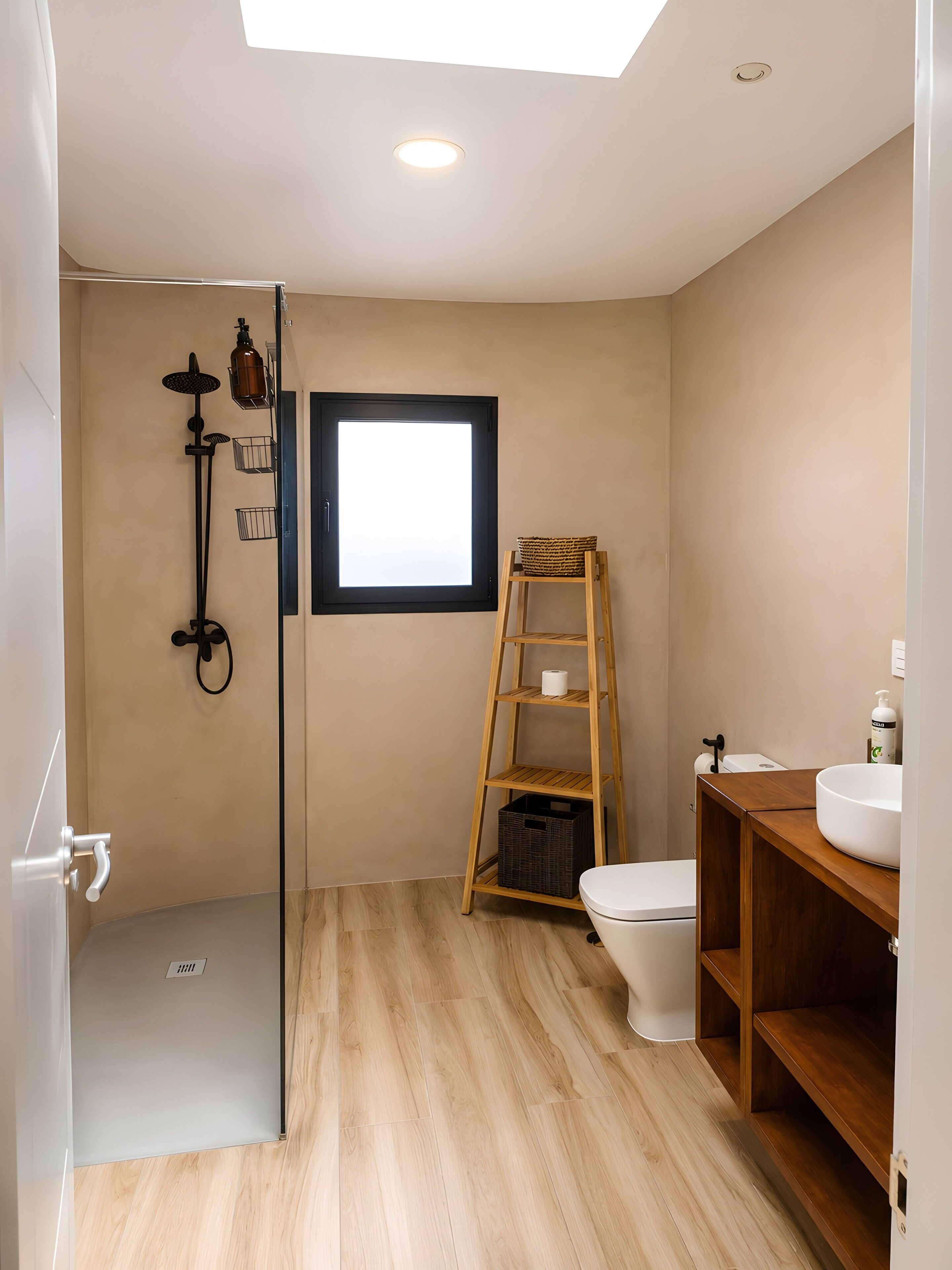 Un baño con ducha, inodoro y lavamanos, suelo de madera y una ventana.