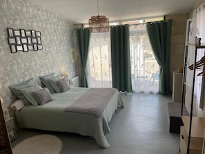 A bedroom with a large bed, a bedside table, a hanging light fixture, and a view through a window with curtains.