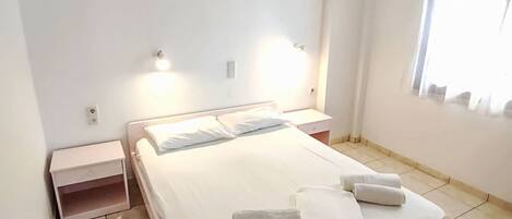 A hotel room with a bed, bedside tables, and a window with curtains.