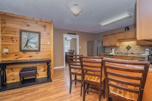 A wooden interior with a dining area, kitchen, and a framed picture on the wall. - 🌲Keaton's Streams and Dreams🔥Creek, Fire Pit & Hot Tub (Sevierville)