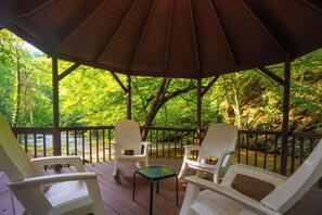 A covered outdoor seating area with two chairs and a table, overlooking a river and surrounded by trees. - 🌲Keaton's Streams and Dreams🔥Creek, Fire Pit & Hot Tub (Sevierville)