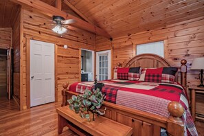 A wooden cabin bedroom with a bed, a bench, a ceiling fan, and a window. - 🌲Keaton's Streams and Dreams🔥Creek, Fire Pit & Hot Tub (Sevierville)