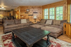 Ein gemütliches Wohnzimmer mit einem Ecksofa, einem Couchtisch und Blick ins Freie durch große Fenster.