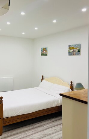 A bedroom with a wooden bed, white bedding, a bedside table, a lamp, and two wall-mounted paintings.
