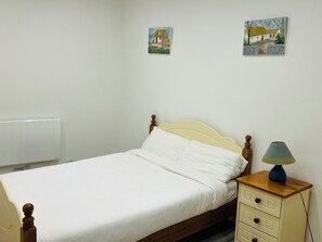 A single bed with a wooden headboard, a bedside table with a lamp, and two wall-mounted paintings.