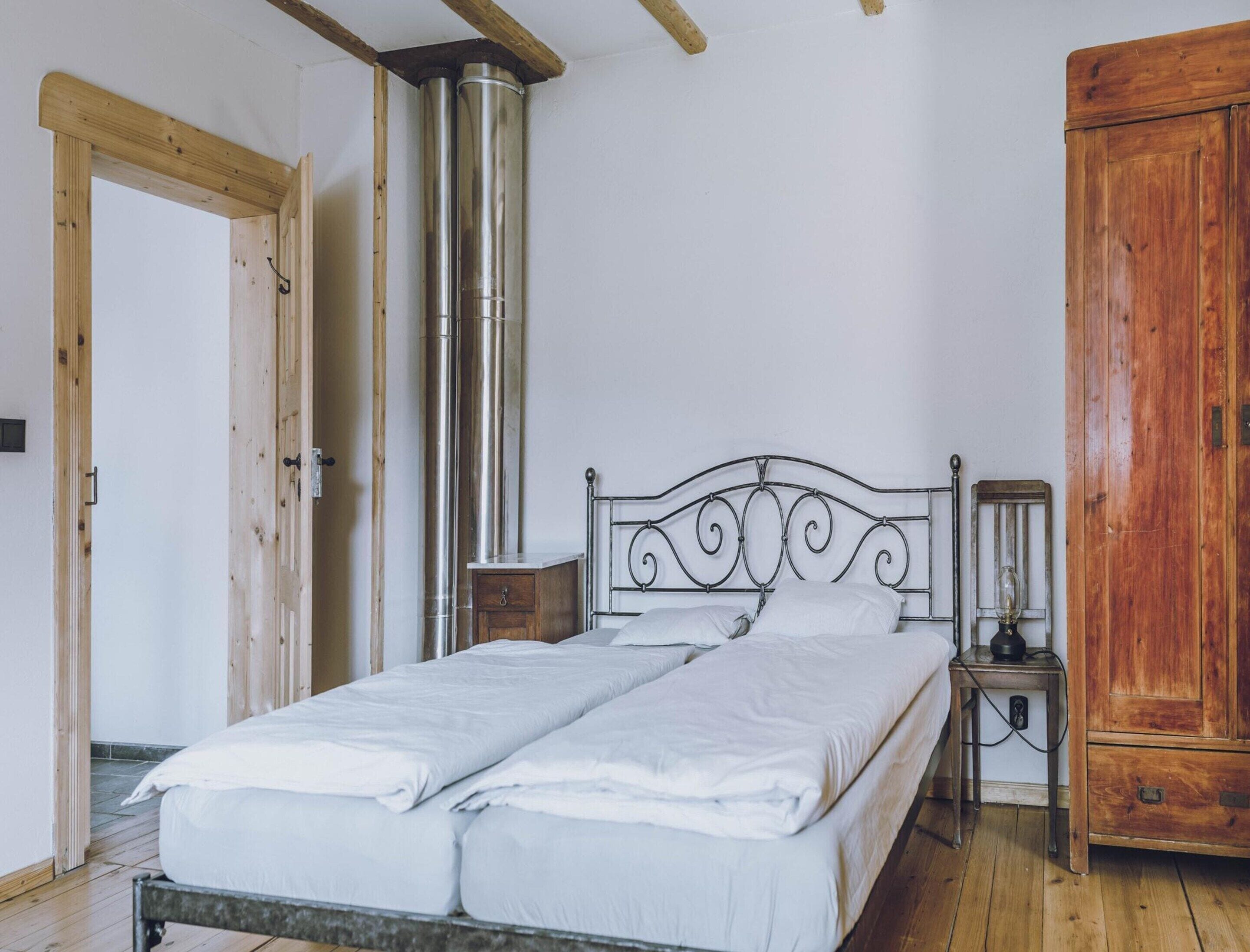 A bedroom with a metal bed frame, a wooden wardrobe, and a wall-mounted heater.