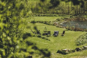 A grassy outdoor area with a pond, surrounded by trees and vegetation. There are several chairs and a table arranged for outdoor dining. - Riverside Flat for Two Guests (Janowice Wielkie)