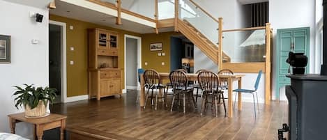 A spacious living area with a wooden staircase, a dining table with chairs, and a kitchen area.
