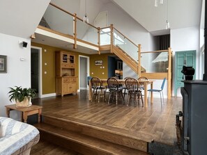 A spacious living area with a wooden staircase, a dining table with chairs, and a kitchen area.