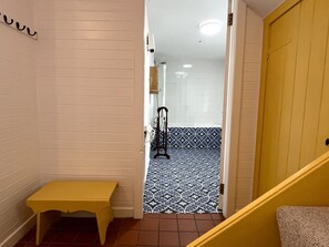 Ein schmales Dielenstreifen mit einer Sitzbank, einer zur Toilette führenden Tür und einem gemusterten Boden.