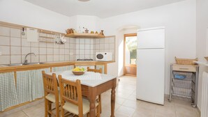 A kitchen with a dining table, chairs, a refrigerator, and a window. - Country Home “Servera” with Pool, Wi-Fi, Terrace & Garden (Santanyí)