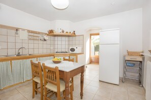 Eine Küche mit Esstisch, Stühlen, einem Kühlschrank und einem Fenster.