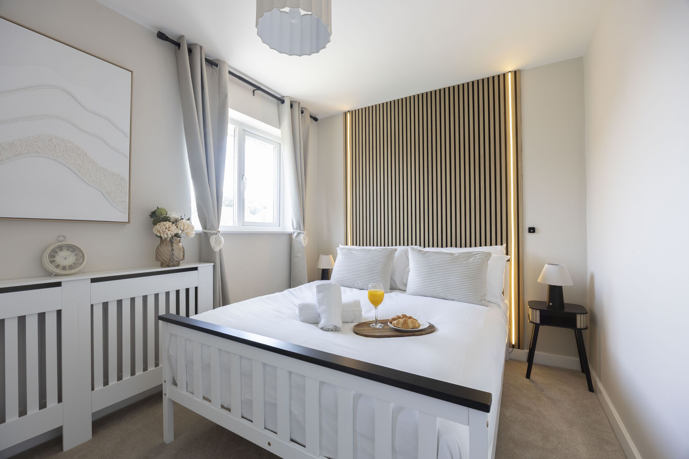 Ett hotellrum med en säng, ett sängbord, en lampa och ett fönster med gardiner.