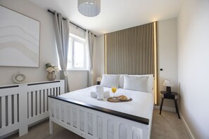 Una habitación de hotel con cama, mesita de noche, lámpara y ventana con cortinas.