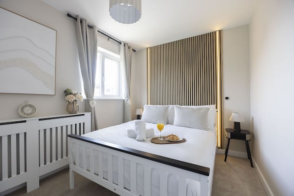 A hotel room with a bed, bedside table, lamp, and a window with curtains.