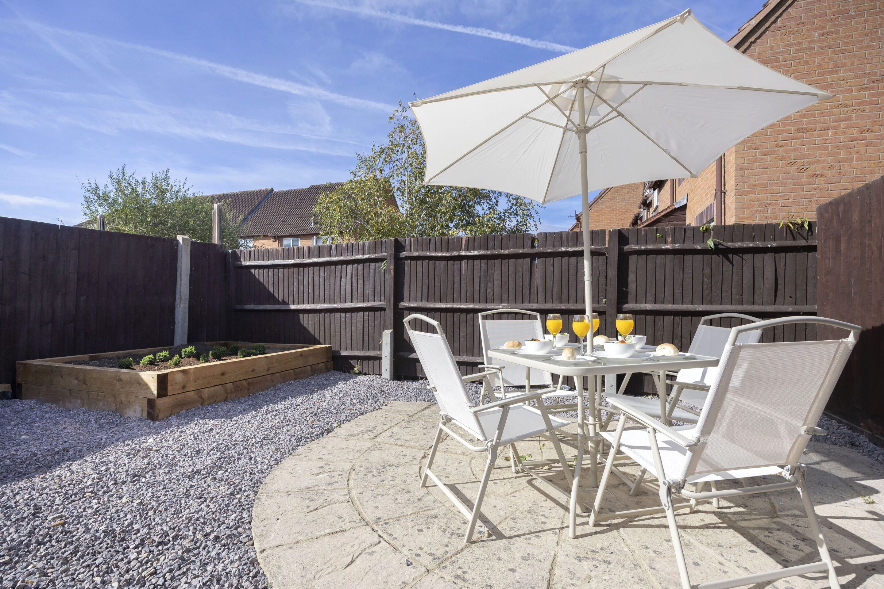 Une terrasse avec une table et des chaises, un parasol et un parterre de fleurs.